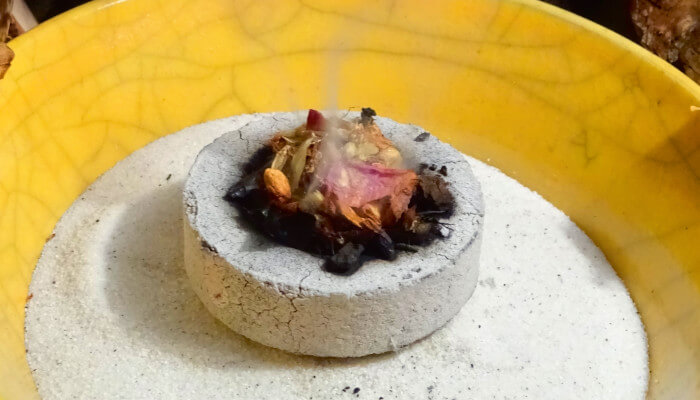 gelbe Schale mit Sand und Räucherstein mit Kräutermischung