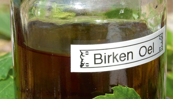 Glas mit brauner Flüssigkeit drin und grünes Blatt davor