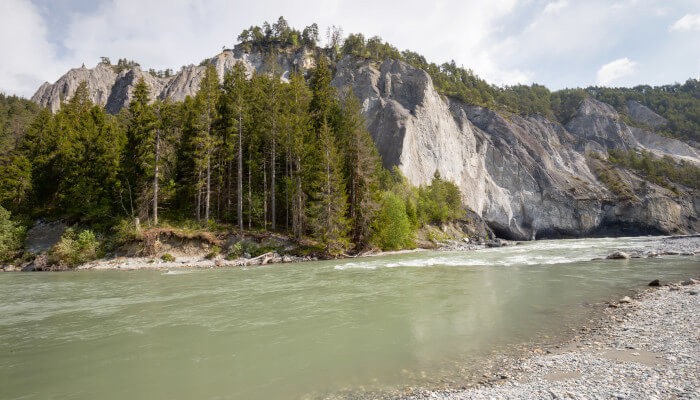 blaugrauer Fluss vor Felswand und Bäumen
